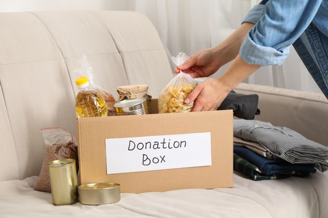 Young woman puts groceries in donation box. Volunteer