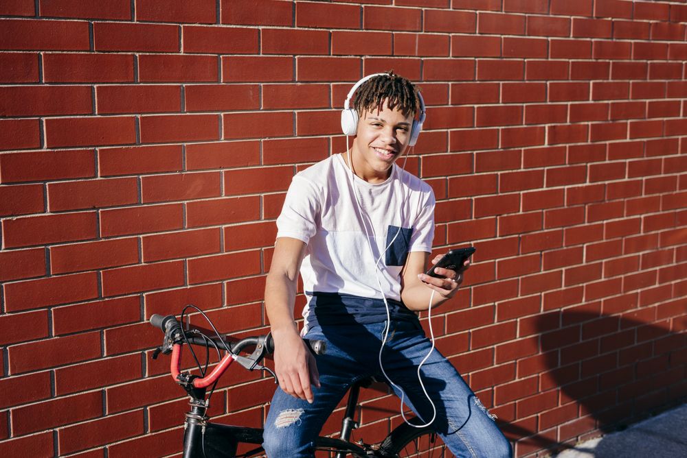 Young happy Black male listening music with smartphone on bike