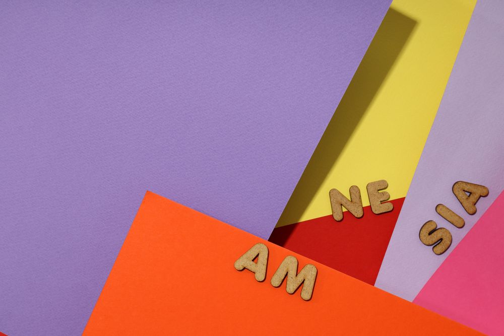 Scattered brown letters spelling “amnesia” on colorful paper background