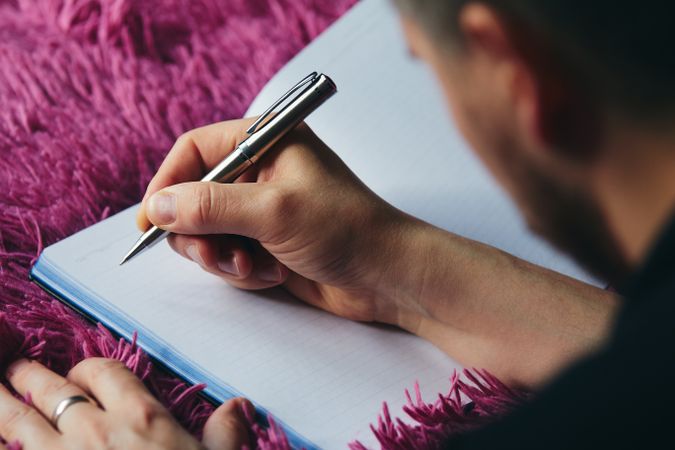 Man Writing in Notebook on Bed