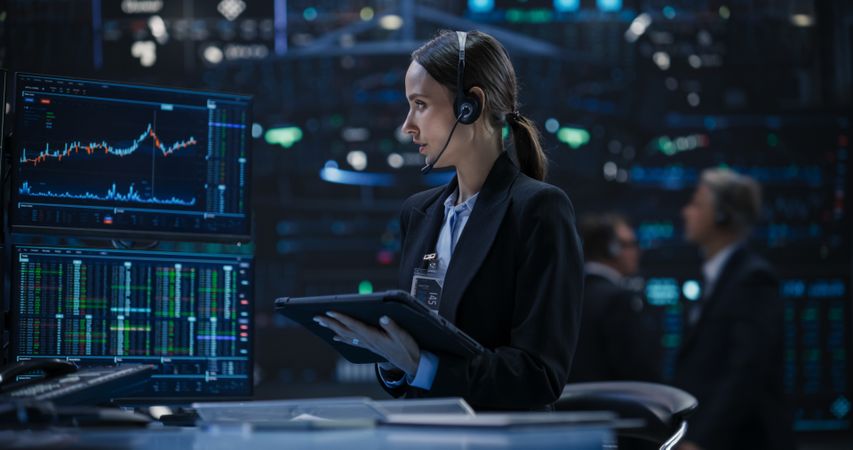 Young Broker Using Tablet Computer in Office, Communicating Buy and Sell Orders while Talking to Clients on a Phone Call