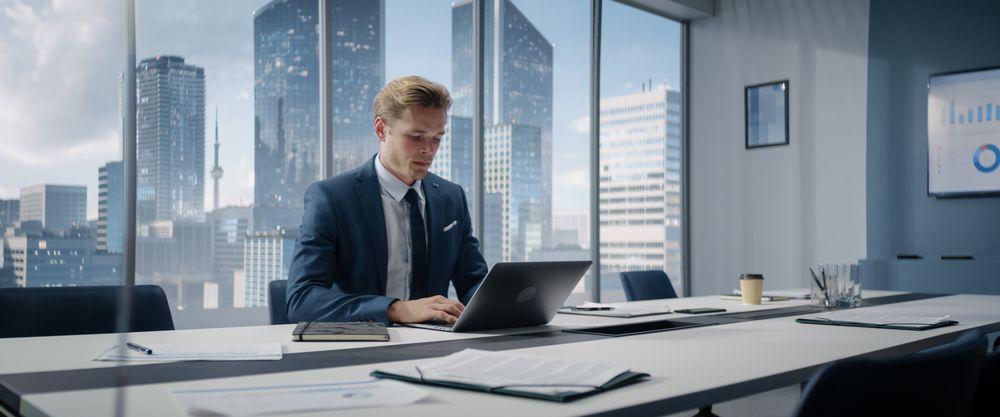 Portrait of Successful White Businessman Working on Laptop Computer in His Big City Corner Office.