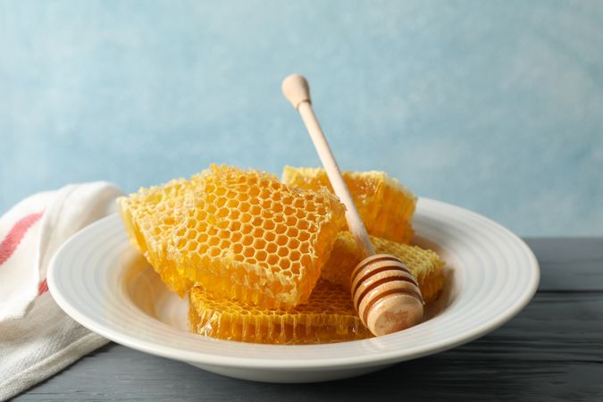 Plate with dipper and honeycombs on wooden background, space for text