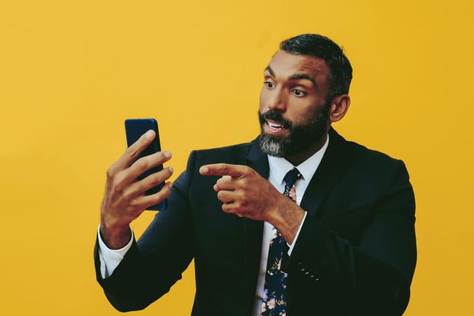Agitated Black businessman in suit speaking at smartphone screen while pointing