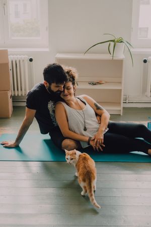 Loving couple cuddling on floor while cat walking around