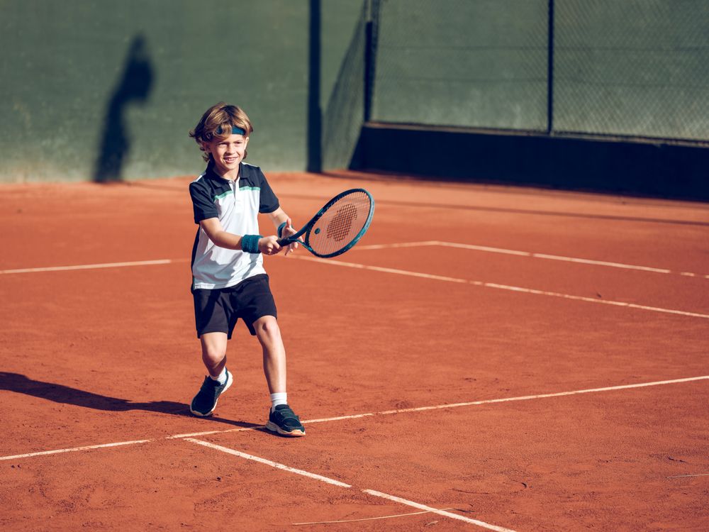 Adorable little boy running to hit ball while playing tennis