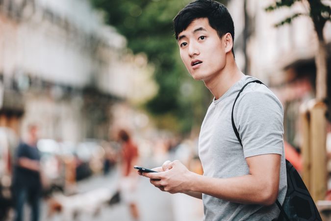 Confused Asian man using smartphone while standing on street