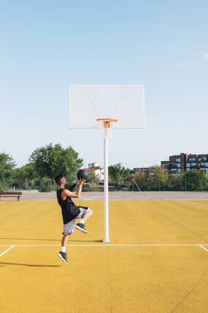 Young man playing on yellow basketball court outdoor.