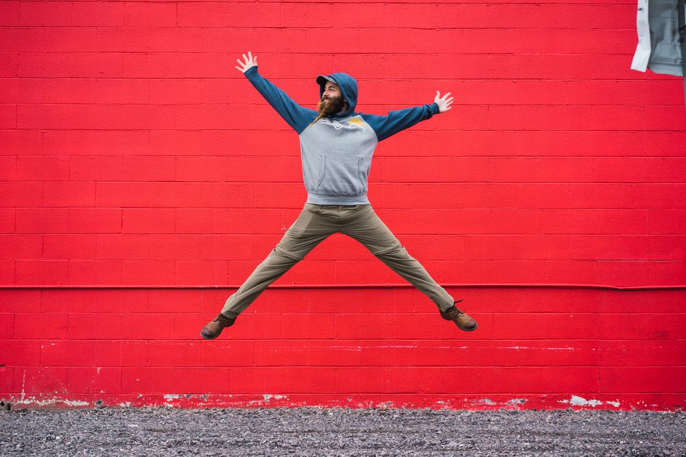 Bearded guy jumping near red wall