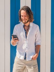 Smiling man browsing smartphone against striped wall