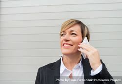 Smiling businesswoman speaking on cell phone in front of wall 41QO84