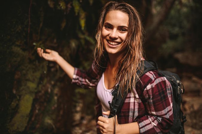 Smiling woman raising her hand near moss covered rocks to feel water drops