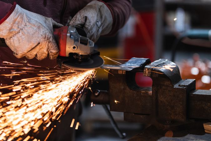 Craftsman grinding metal with grinder in vice