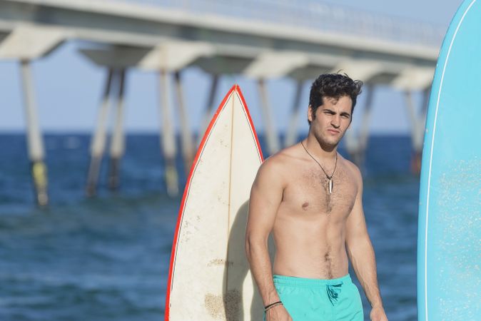 Mid shot of male surfer standing with two boards and looking at camera