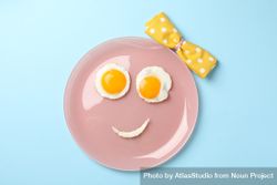 Looking down at pink plate with smiley face on it made of eggs and condiments 5a6Ja4