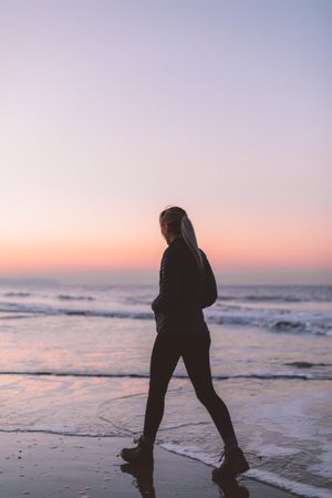Silhouette of woman walking on beach during sunset