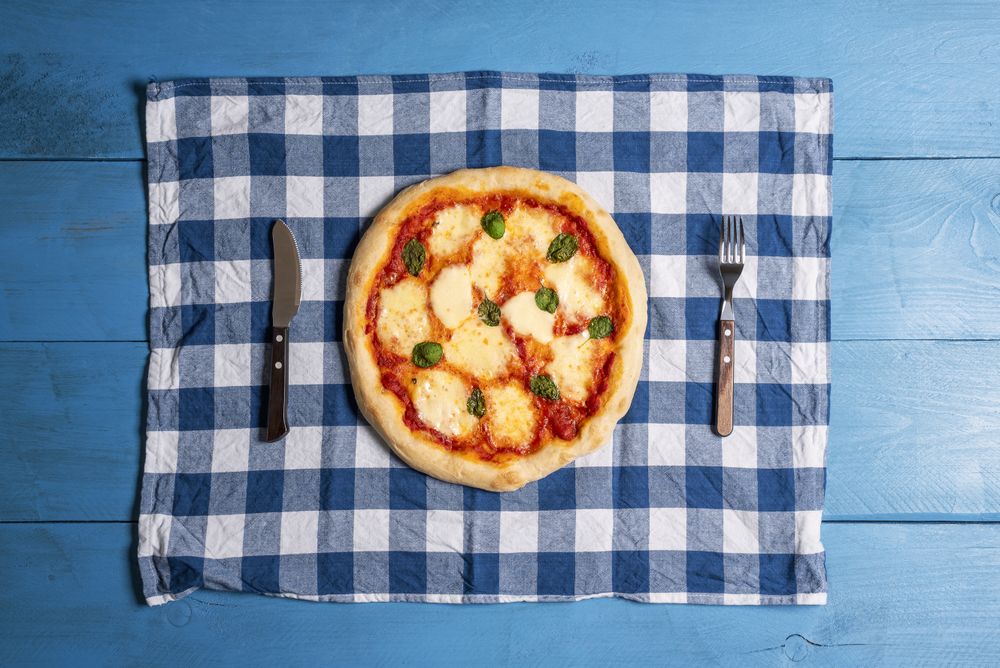 Overhead of whole margherita pizza on a blue table