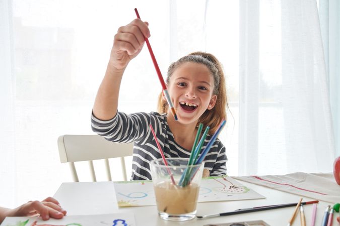 Cheerful girl with paintbrush at table
