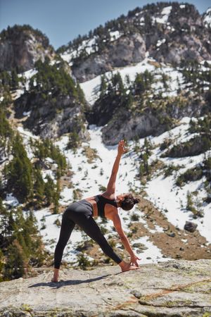 Woman doing extended triangle yoga pose outside on sunny day in the mountains