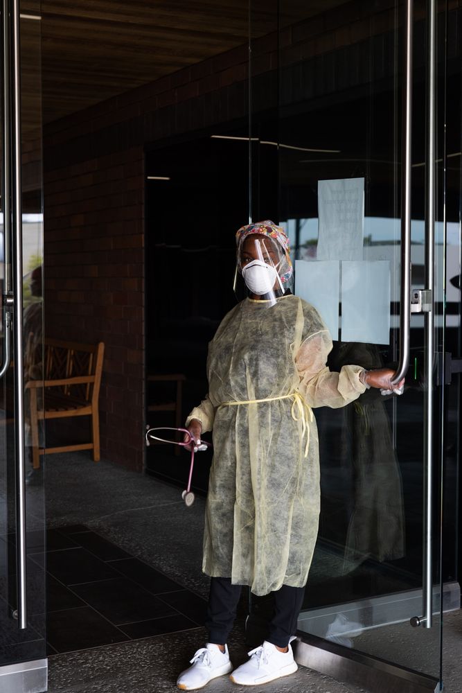 Nurse in PPE holding building door open