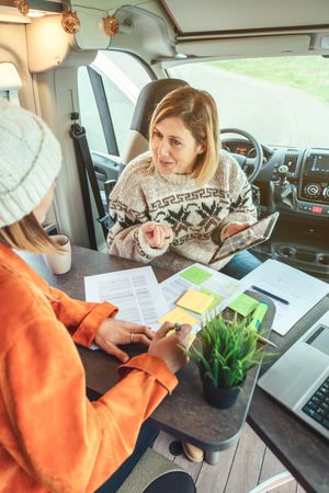 Female friends working remotely in back of van while on a road trip, vertical
