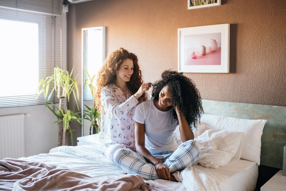 Woman combing another female's hair in bed
