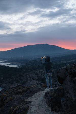 Male taking photo with smartphone on cliff at dusk