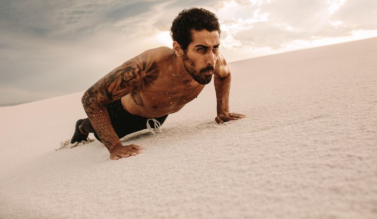Fit man doing push-ups over sand dunes