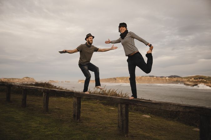 Couple holding hands and jumping on bench on shore near water