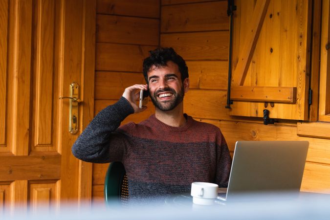 Cheerful man speaking on smartphone and working on terrace