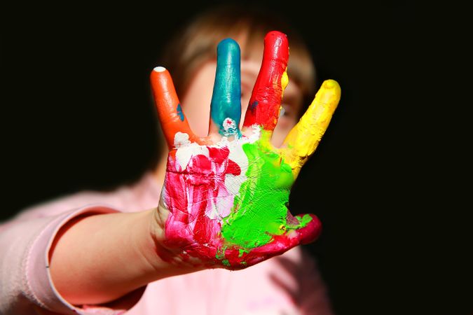 Close up of finger painted child hand with girl in background
