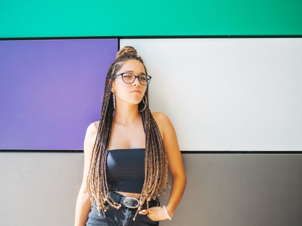 Charming teenage girl with braids in sunglasses nearby colorful wall