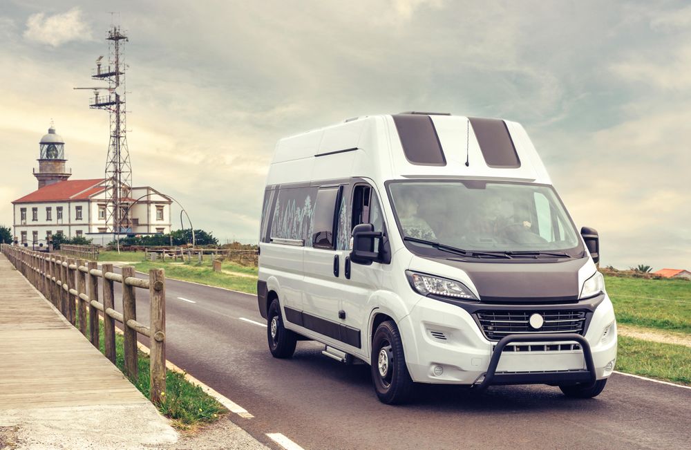 Camper van driving on road away from lighthouse on overcast day