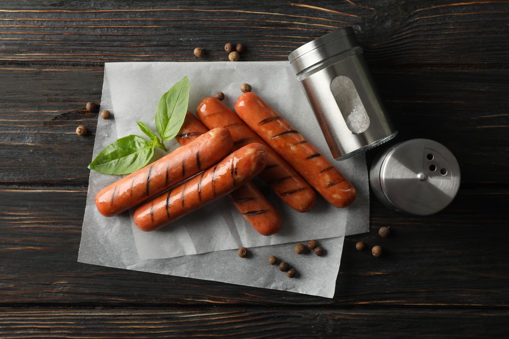 Grilled sausages or hot dogs with capers and basil, top view