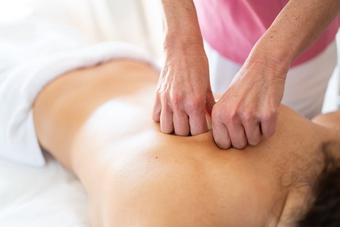Massage therapist using fists while massaging back of female patient