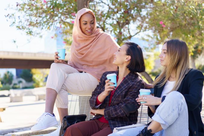 Three women sitting on outdoor park bench with to go beverages