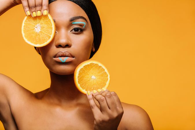 Close up of woman with vivid makeup and orange slices in hand