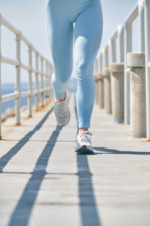 Crop jogger running on bridge over sea during cardio training