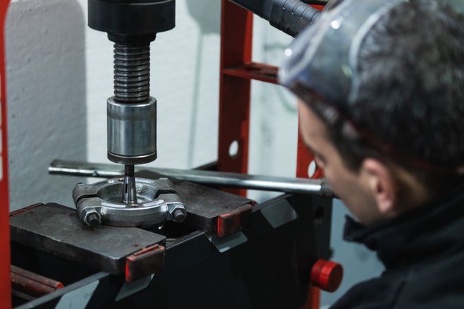 Concentrated man working hydraulic press in garage