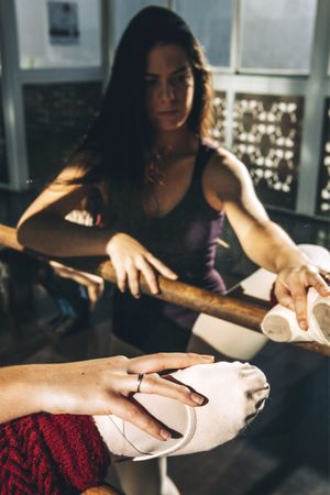 Concentrated woman in pointe shoes warming up with barre in front of mirror.