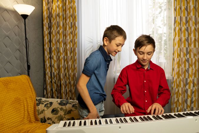 Two boys playing the piano together in cozy home setting