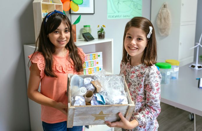 Two girls in ecology classroom showing box of waste to recycle