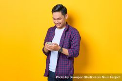 Happy Asian man in plaid shirt  looking down at smartphone 41Kwp0