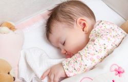 Baby sleeping soundly in a cot with pacifier and toy