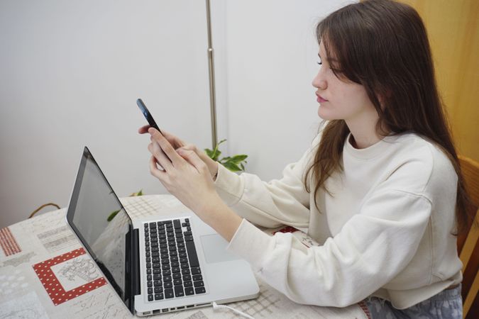 Side view of teenage girl using smartphone and computer