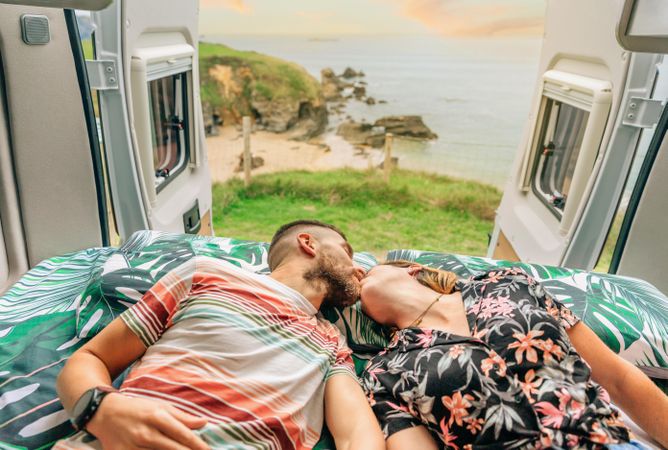 Male and female kissing on bed in motorhome with door open