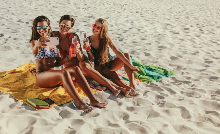Women on vacation at a beach posing for a selfie wearing sunglasses