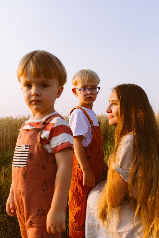 Adorable little kids standing near content young mom in agricultural field
