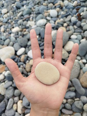 Hand Holding a Flat Stone on Rocky Beach