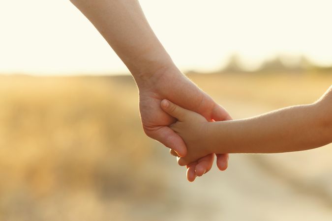Adult and child holding hands with field in background